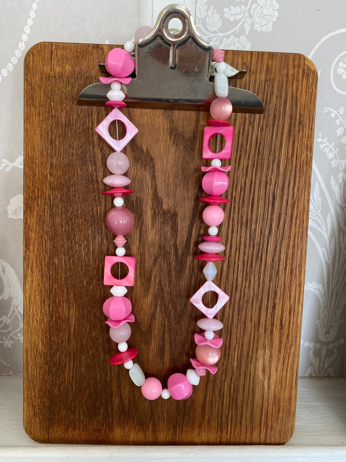 Bold and playful sixties-inspired necklace featuring an eclectic mix of chunky beads in shades of pink, white, and coral, with geometric accents and glossy finishes.